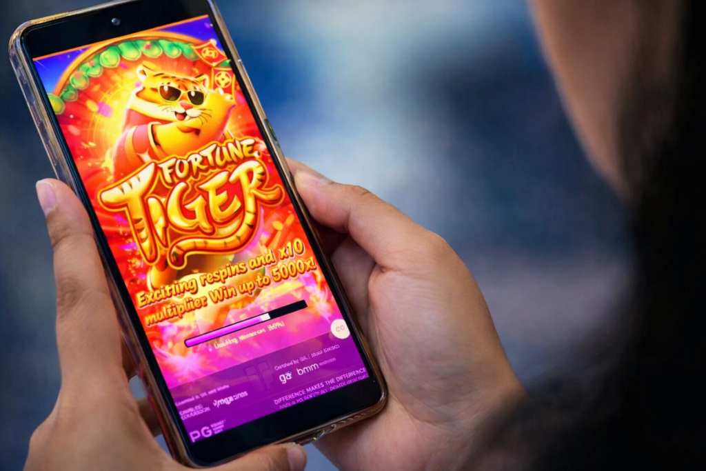 Pessoa segurando smartphone com o jogo Fortune Tiger aberto na tela, slot online popular com tema asiático, cores vibrantes e destaque para ganhos e multiplicadores.